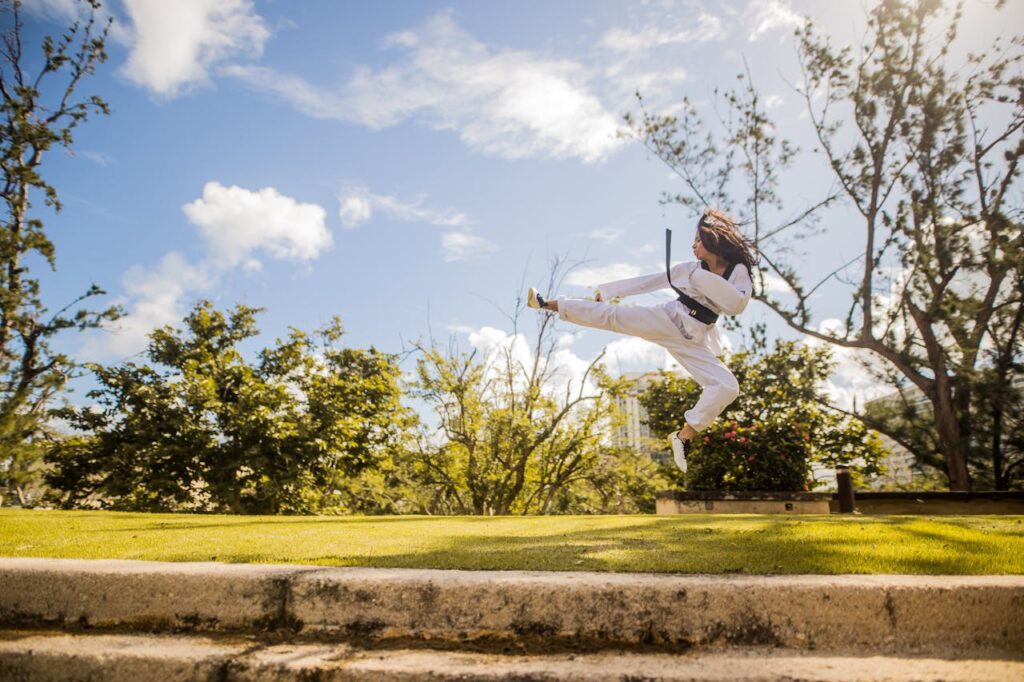 pexels photo 3023756 Young woman performs a martial arts kick in a sunny park, showcasing athleticism and focus.